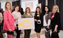 Шість жінок з бейджами тримають плакат у руках.