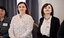 Дві жінки у діловому одязі сидять у приміщенні.