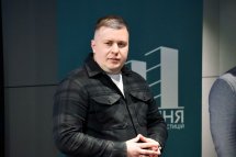 Чоловік у темному одязі стоїть у приміщенні.