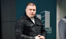 Чоловік у темному одязі стоїть у приміщенні.