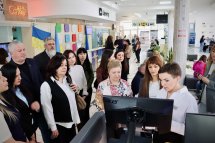 Група людей перебувають біля комп'ютера, у приміщенні.