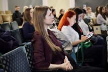 Жінка уважно слухає виступ, позаду неї інші учасниці.