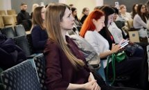 Жінка уважно слухає виступ, позаду неї інші учасниці.