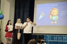 Хлопець з мікрофоном та дві жінки на сцені перед екраном.