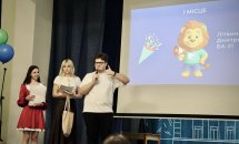 Хлопець з мікрофоном та дві жінки на сцені перед екраном.