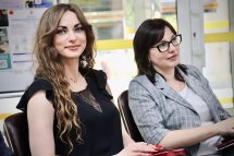 Дві жінки сидять у приміщенні та посміхаються.