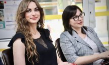 Дві жінки сидять у приміщенні та посміхаються.