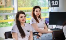 Дві жінки у білому одязі сидять у приміщенні та посміхаються.