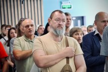 У приміщенні багато людей тримають руку на серці.