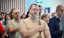 У приміщенні багато людей тримають руку на серці.