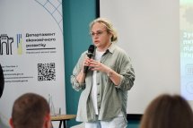 Жінка зі світлим волоссям, в окулярах, тримає мікрофон у руках.