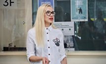 Жінка зі світлим волоссям, в окулярах, щось розповідає у приміщенні.