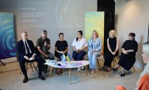 Група людей сидить на презентації, перед ними стіл з прапорцями України.