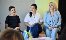 Три жінки сидять у приміщенні та посміхаються.