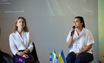 Дві жінки сидять на сцені, одна з мікрофоном. На столику перед ними — прапорці України та Швеції.
