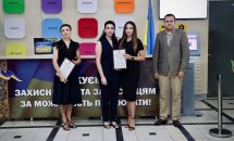 Троє жінок в чорному одязі та чоловік позують для фото, дві жінки тримають грамоти.