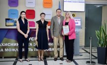 Три жінки та чоловік позують для фото, одна жінка тримає грамоту.