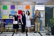 Троє жінок та чоловік позують для фото, дві жінки тримають грамоти.