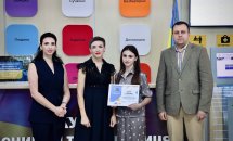 Три жінки в темному одязі та чоловік позують для фото, одна жінка тримає подяку.