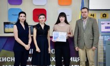 Три жінки з темним волоссям та чоловік позують для фото, одна жінка тримає подяку.