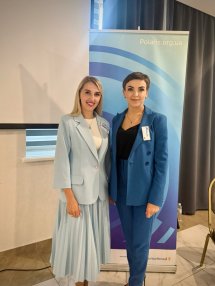 Дві жінки в діловому одязі позують для фото у приміщенні.