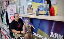 Біля стійки сидить чоловік у візку, поруч стоїть жінка.