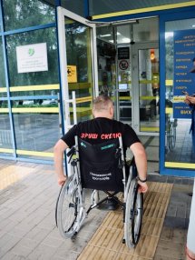 Чоловік на кріслі колісному біля входу у приміщення.