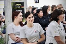 Люди сидять у залі у білих та чорних футболках та уважно слухають