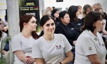Люди сидять у залі у білих та чорних футболках та уважно слухають