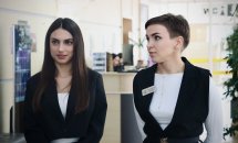 Дві жінки у діловому одязі перебувають у приміщенні.