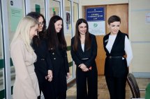 П'ять жінок стоять у приміщенні та посміхаються.