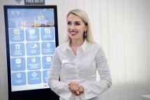 Жінка у білій сорочці посміхається, перебуваючи у приміщенні