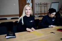 Жінка із світлим волоссям сидить за столом та посміхається.