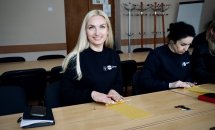Жінка із світлим волоссям сидить за столом та посміхається.