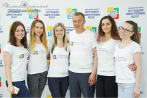 П'ять жінок та чоловік у білих футболках позують на фоні банера.