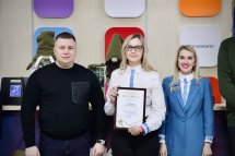 Троє людей стоять разом, жінка по центру тримає подяку.