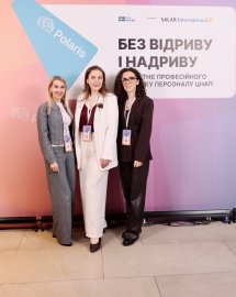 Три жінки стоять біля банера