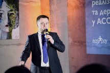 Чоловік у діловому костюмі тримає мікрофон у руках.