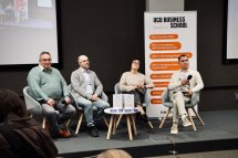 Жінка та троє чоловіків сидять перед екраном та банером.