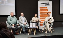 Жінка та троє чоловіків сидять перед екраном та банером.