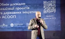 Чоловік у картатому піджаку говорить у мікрофон.