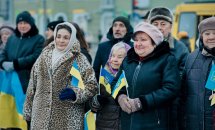 Люди у верхньому одязі тримають прапорці України