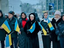 Жінки у верхньому одязі тримають прапори України у руках.