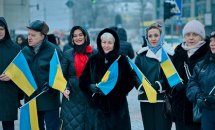 Жінки у верхньому одязі тримають прапори України у руках.