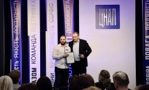 Чоловік в білій сорочці тримає подяку, чоловік в чорному піджаку стоїть поряд