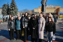 Група жінок стоять на вулиці, на фоні - пам'ятник.