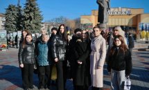 Група жінок стоять на вулиці, на фоні - пам'ятник.