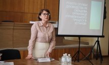Жінка в окулярах стоїть у приміщенні.