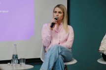 Жінка зі світлим волоссям сидить на стільці та тримає у руках мікрофон.