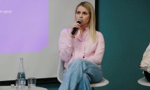 Жінка зі світлим волоссям сидить на стільці та тримає у руках мікрофон.